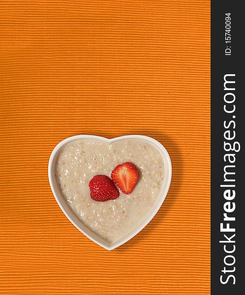 Strawberries in a heart shaped bowl on a bright orange canvas background