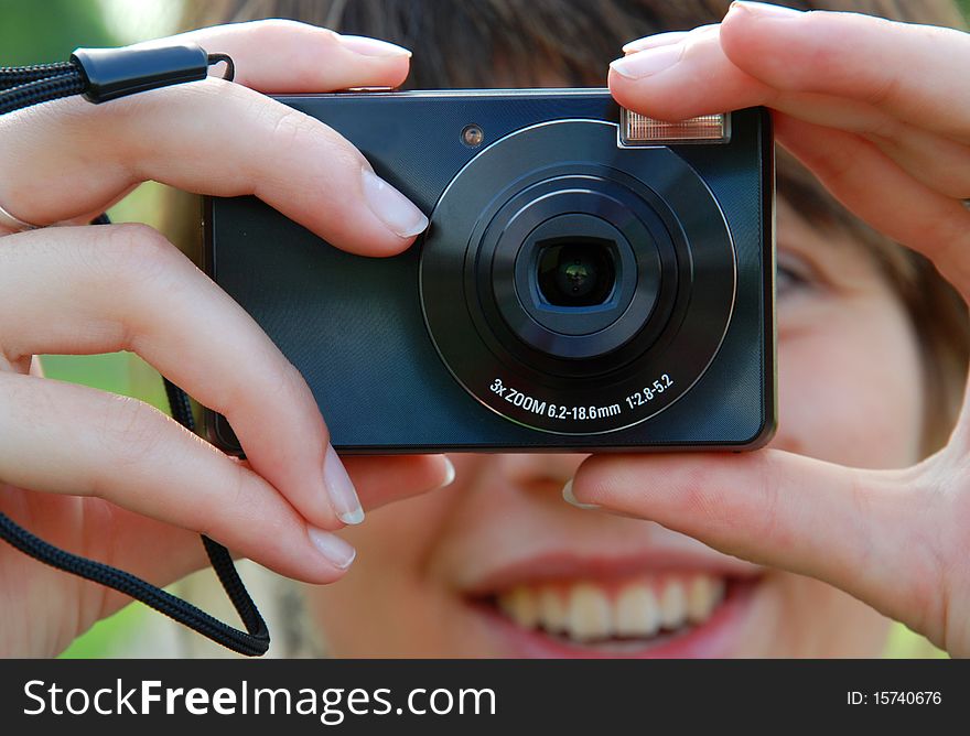 Smiling girl is holding the camera in hands. She is taking a photo.