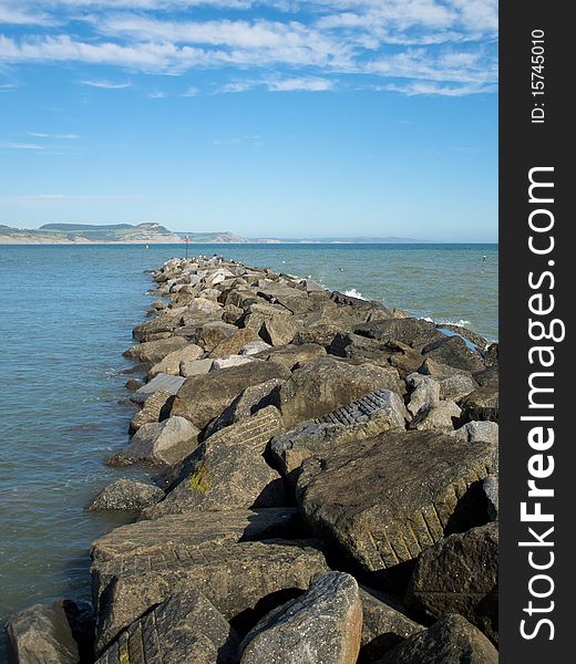 A stone water brake stretching out across the bay. Cliffs in the background with whispery clouds in the sky. Was taken in Lyme Regis, UK