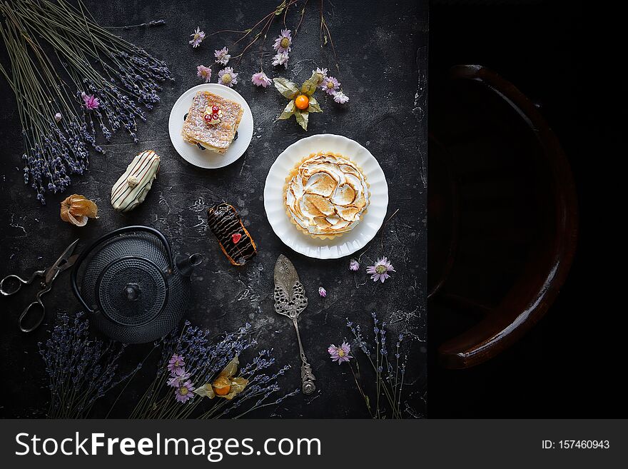 Tea And Sweets On A Dark Background, Mille-feuille, Eclairs, Tart, Decorative With Flowers, Top View, Vintage