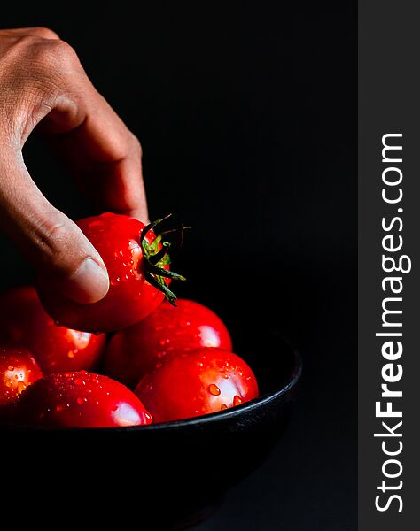 Hand hoilding Fresh red tomato in wooden cup healthy food and vegetable concept on black background