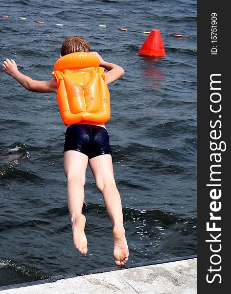 The child in a life jacket jumps in a reservoir.