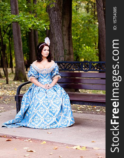 A portrait of lady in a blue baroque dress sitting on bench. A portrait of lady in a blue baroque dress sitting on bench
