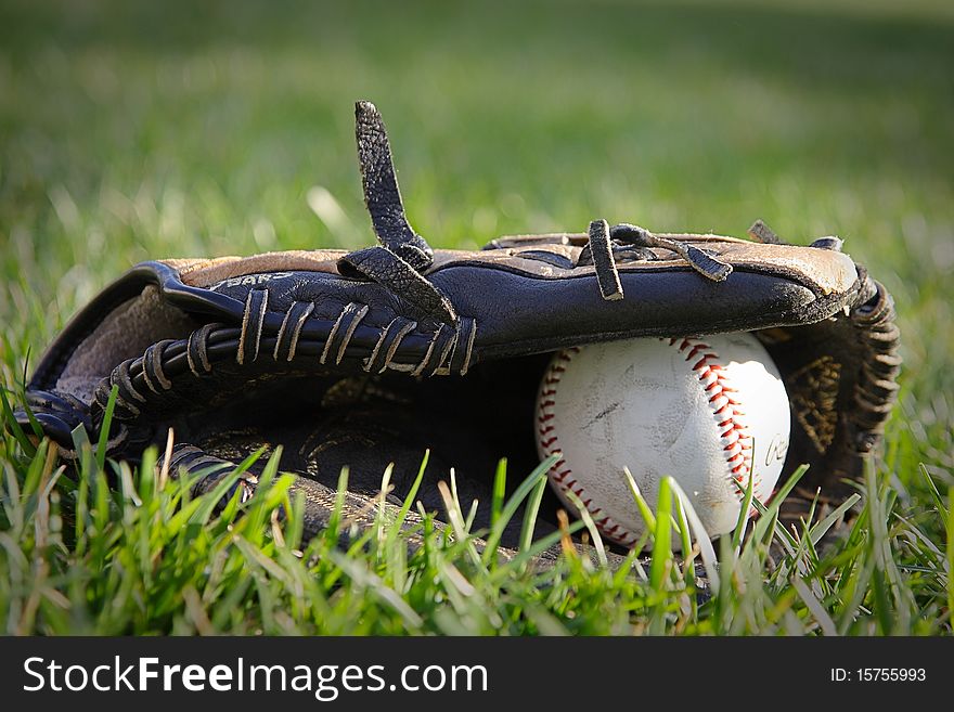 A baseball and glove laying in the grass on a field. A baseball and glove laying in the grass on a field.