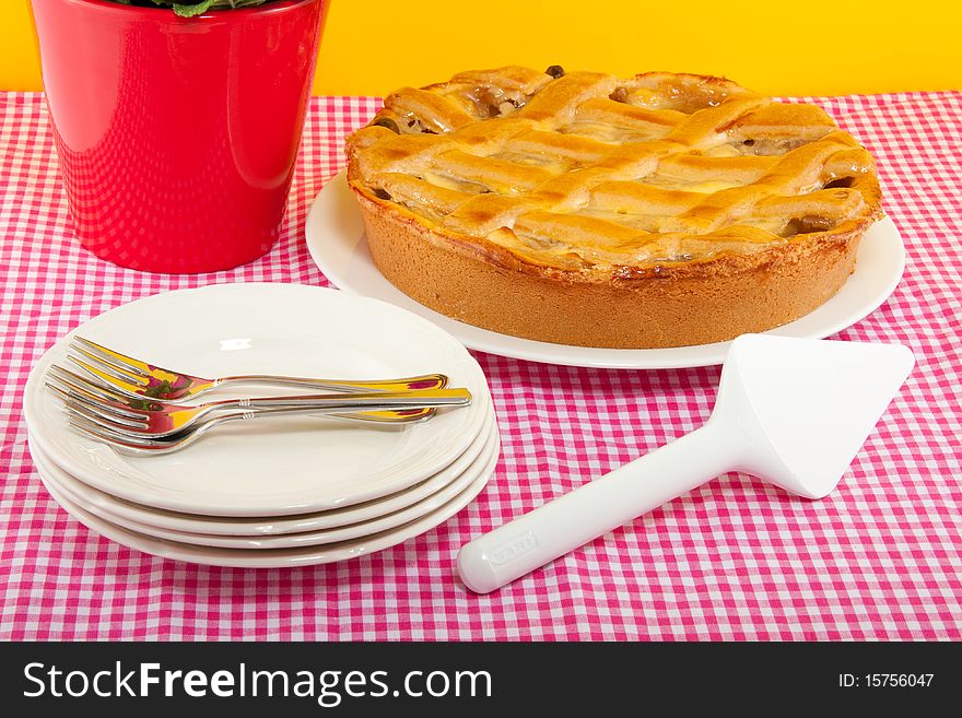 An apple pie on a pink white checkered tablecloth with service and forks