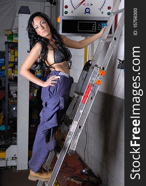 Photograph showing sexy young woman in bikini top and overalls stood on ladders