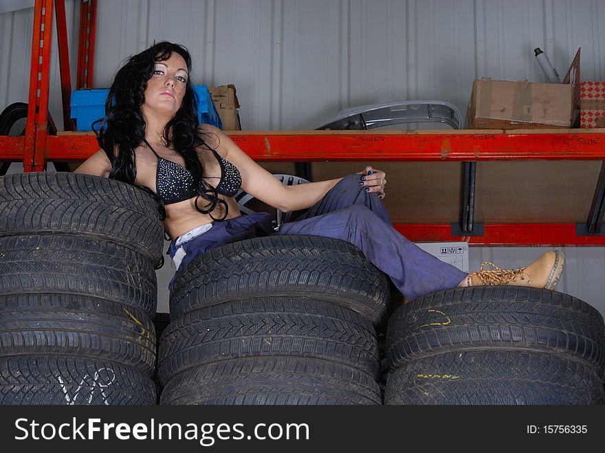 Photograph showing sexy young woman in bikini top and overalls posing on tyres. Photograph showing sexy young woman in bikini top and overalls posing on tyres