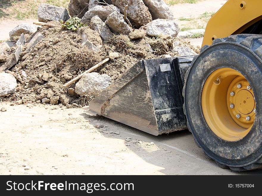 Little yellow excavator shovels the soil from a road on a warm summer day. Little yellow excavator shovels the soil from a road on a warm summer day