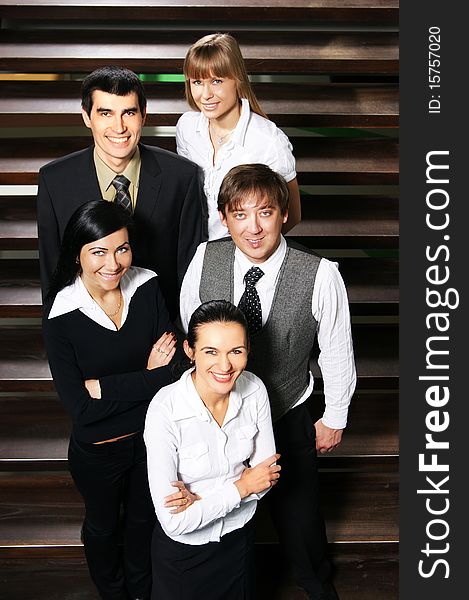 Five young business people are standing as a team with a lovely woman in front. The image is taken on the stairs.