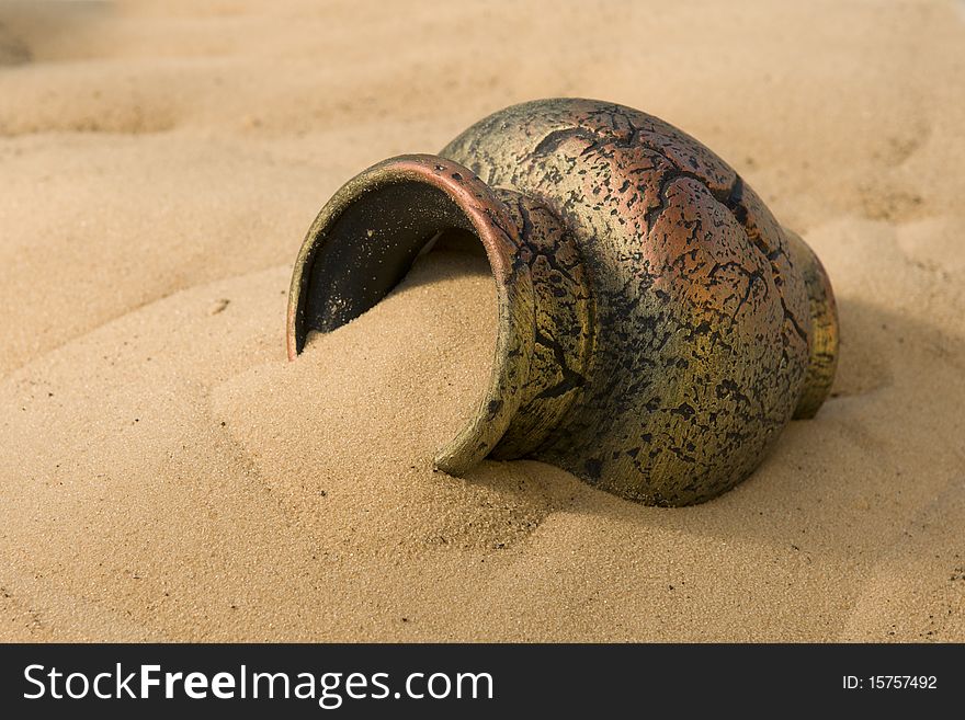 The ancient clay amphora lies on a surface of yellow sand