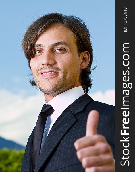 Young businessman with thumb up sign over a blue sky in the background. Young businessman with thumb up sign over a blue sky in the background.