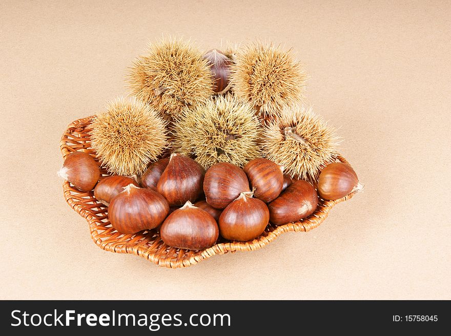 Sweet chestnuts and chestnut husks. Studio shot over a light brown background