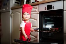 Little Girl In A Red Cook Suit Plays With Kitchen Utensils Near The Oven. Playing In The Kitchen Close Up Stock Image
