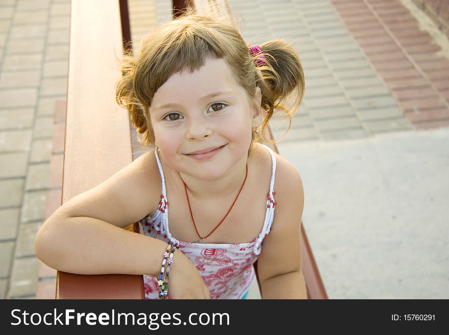 The lovely girl sits on a bench and charmingly smiles. The lovely girl sits on a bench and charmingly smiles