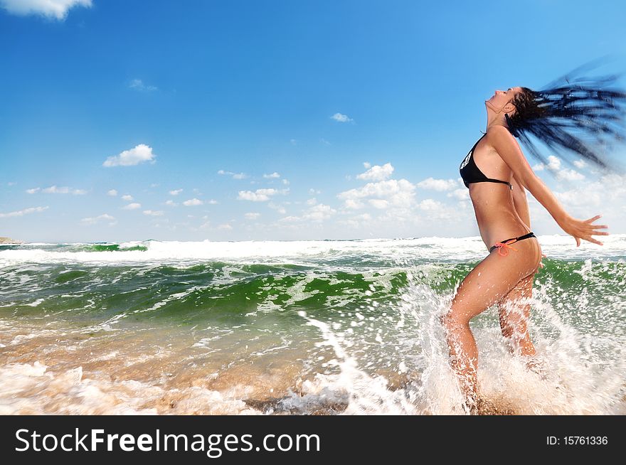 Beautiful girl splashing in the ocean, blue sky