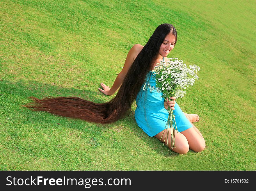 Beautiful woman with long hair sitting on the grass and enjoying nature