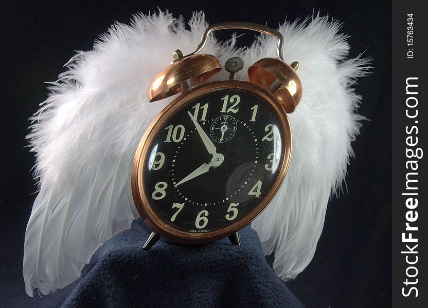 An alarm clock with white feathered wings seems poised to fly away. An alarm clock with white feathered wings seems poised to fly away.