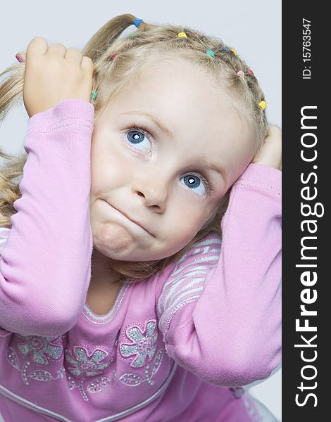 Cute young blond caucasian little girl sitting with playiful expression and looking up holding hair tails in hands isolated. Cute young blond caucasian little girl sitting with playiful expression and looking up holding hair tails in hands isolated