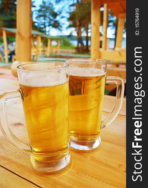 Two mugs of beer staing on the wood table in outside bar. Two mugs of beer staing on the wood table in outside bar.