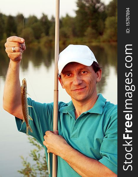 A happy man with a fish and a rod at a river. A happy man with a fish and a rod at a river