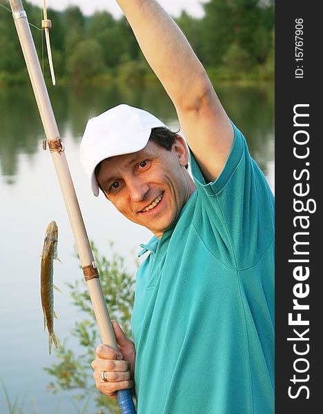 Smiling happy fisherman with a rod and a fish at a river. Smiling happy fisherman with a rod and a fish at a river