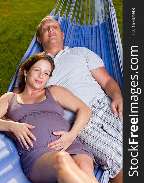 Young loving couple in a hammock in a summer setting. The woman is pregnant. Young loving couple in a hammock in a summer setting. The woman is pregnant.