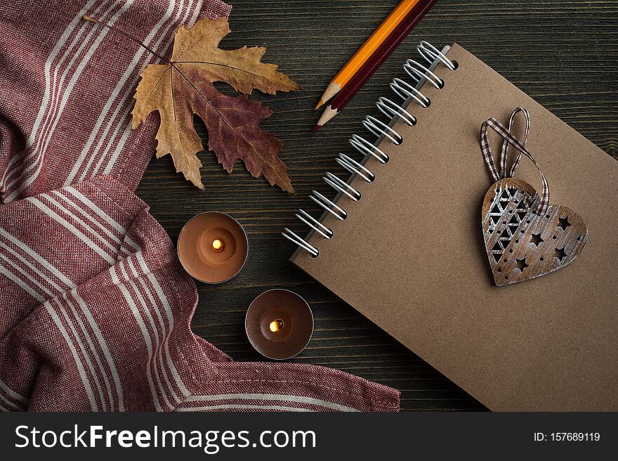 Dark wooden background with autumnal leaves and lit candles, top view with copy space