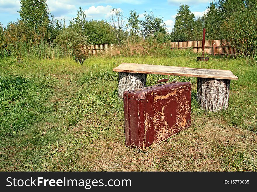 Old valise near wooden bench