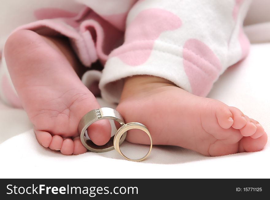 Wedding rings on the toes of a baby girl wearing white and pink clothes