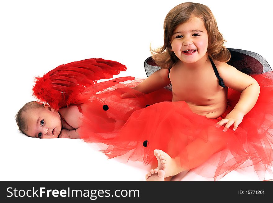 Two sisters playing and smiling in studio wearing red angle wings