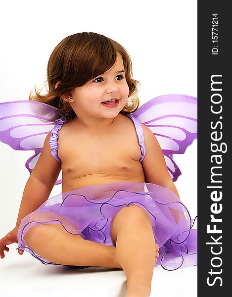 Little girl with purple angle wings sitting in studio and smiling. Little girl with purple angle wings sitting in studio and smiling