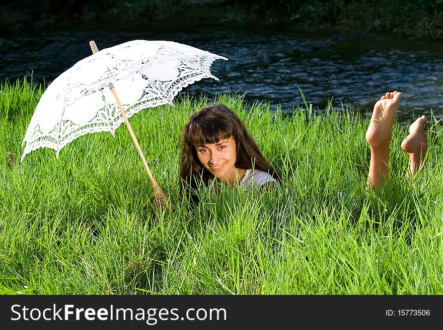 Young  beautiful girl  with sun umbrella relaxing in the fresh green grass near the river. Young  beautiful girl  with sun umbrella relaxing in the fresh green grass near the river