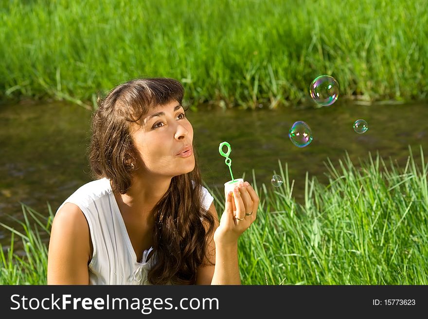 Young nice girl blowing bubbles on the meadow near the water