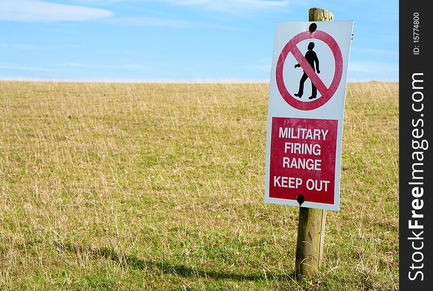 A scratched and worn red and white keep out sign on a wooden post in a field of green grass with blue sky. Focus on the sign.