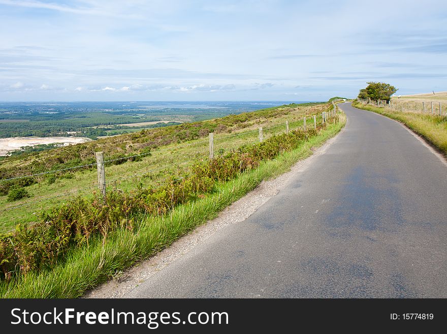 A road winds around the edge of the top of a hill in England on a cloudy summer afternoon. A road winds around the edge of the top of a hill in England on a cloudy summer afternoon.