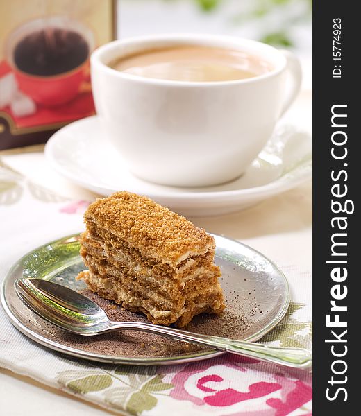 Slice of honey cake on a plate with cherry and coffee in background. Slice of honey cake on a plate with cherry and coffee in background.