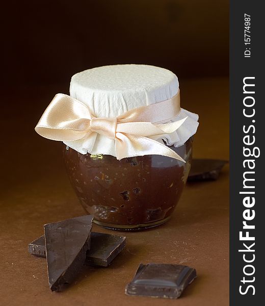 Chocolate marmalade in jar with ribbon on brown background