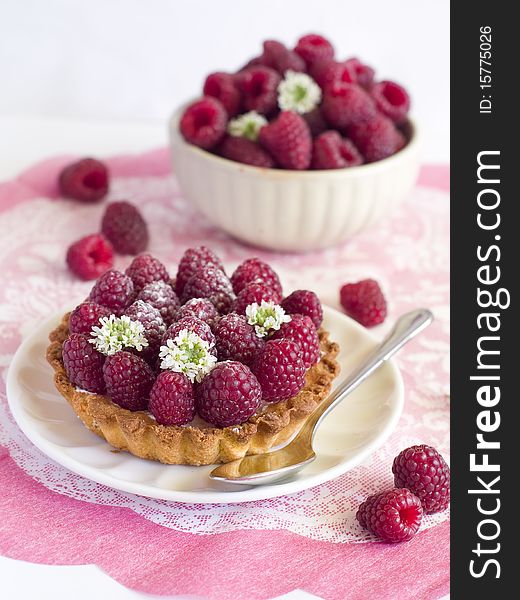 A fresh raspberry tart on a napkin and bowl of raspberries in background