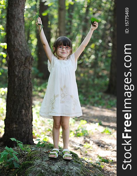 Nice toddler girl in glasses and white dress in the summer forest with hands up. Nice toddler girl in glasses and white dress in the summer forest with hands up