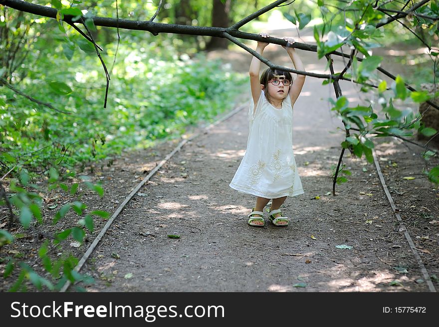 Nice toddler girl in glasses and white dress in the  summer forest playing with tree. Nice toddler girl in glasses and white dress in the  summer forest playing with tree