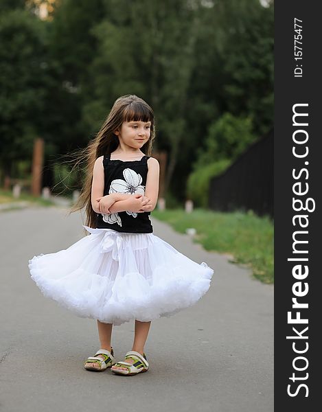 Adorable toddler girl with very long dark hair on the road in white tutu skirt