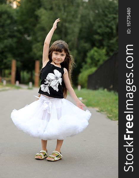 Adorable toddler girl with very long dark hair on the road  dancing in white tutu skirt