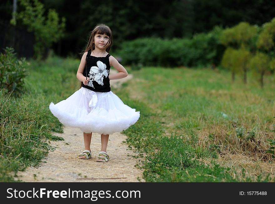 Adorable toddler girl in white tutu skirt with very long dark fluttering hair on country road. Adorable toddler girl in white tutu skirt with very long dark fluttering hair on country road