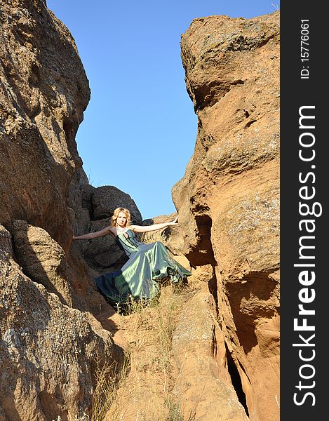 Attractive woman in long green dress siting in the stony ravine. Attractive woman in long green dress siting in the stony ravine