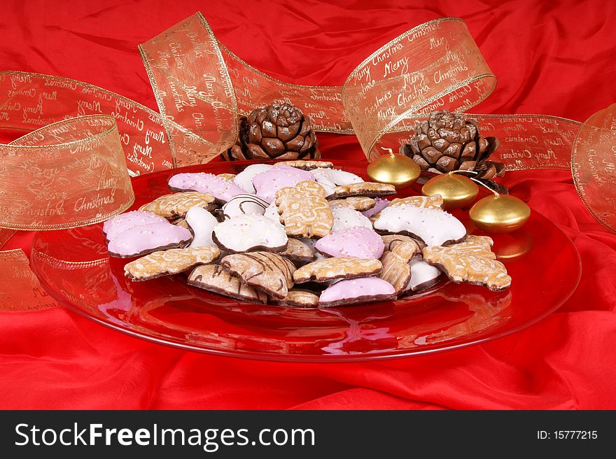 Gingerbread cookies in a red plate with gold candles, pine cones and Christmas ribbon. Studio shot over red background. Gingerbread cookies in a red plate with gold candles, pine cones and Christmas ribbon. Studio shot over red background
