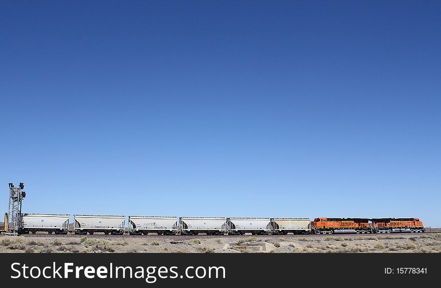 Two engines pulling a long freight train, are seen under an expanse of bright blue sky in a rural location. Two engines pulling a long freight train, are seen under an expanse of bright blue sky in a rural location.