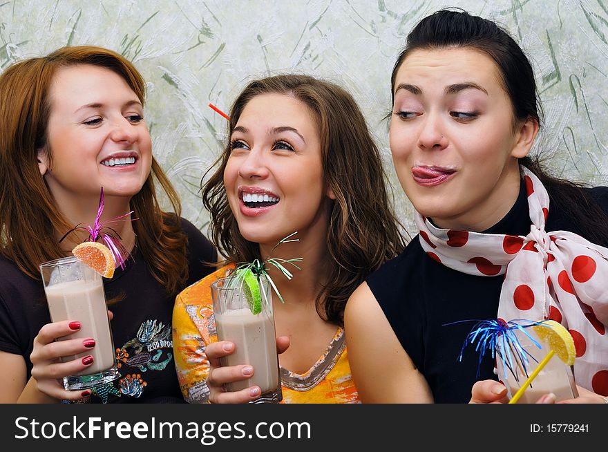 Three beautiful joyful young girls drink cocktails with fruits
