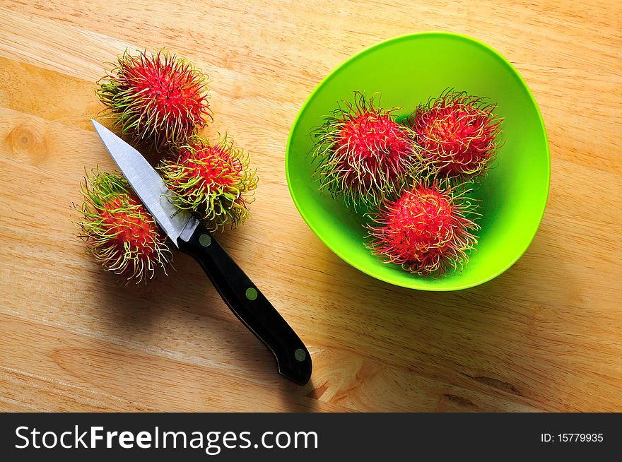 Fresh rambutans in green dish with knife as probs.