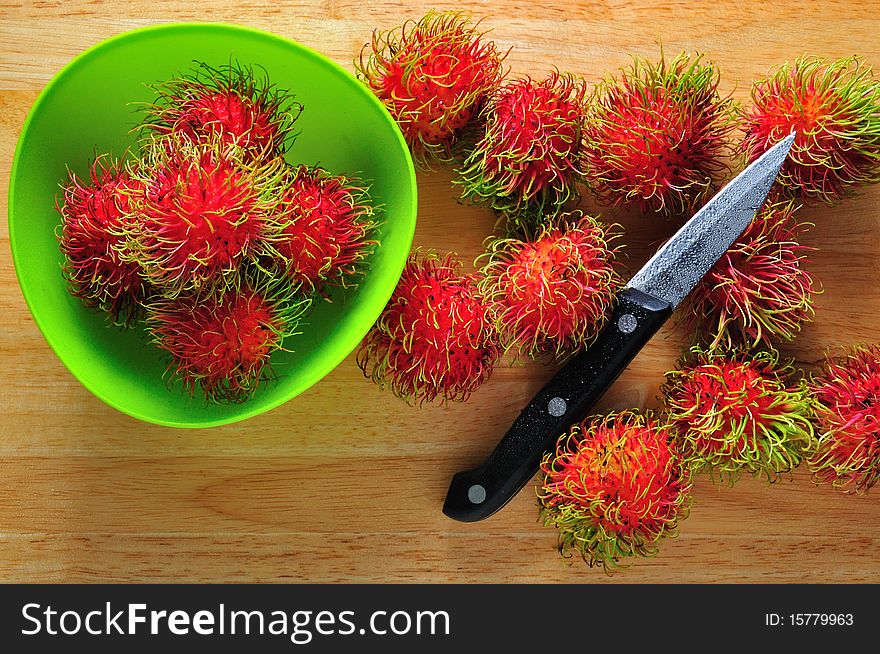 Fresh rambutans in green dish with knife as probs.