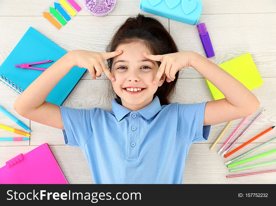 Cute little girl with school stationery on wooden background, top view